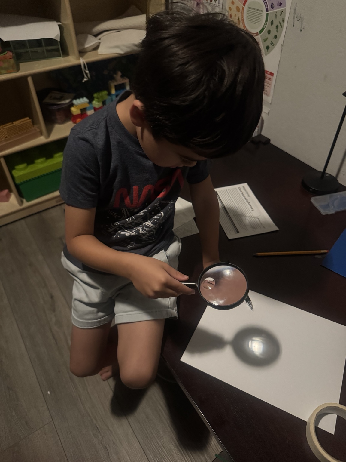 A child holds a magnifying glass above paper to focus the small image of the letter